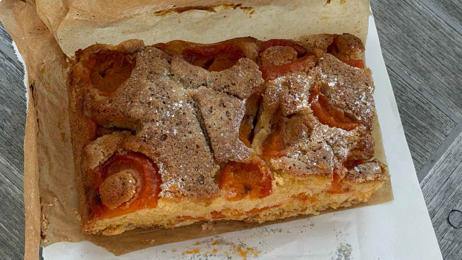A freshly baked artisanal cake dusted with sugar sits wrapped in paper on a wooden table