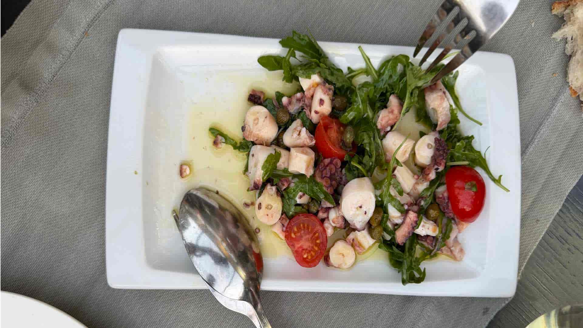 octopus salad in olive oil dressing, served with arugula and cherry tomatoes