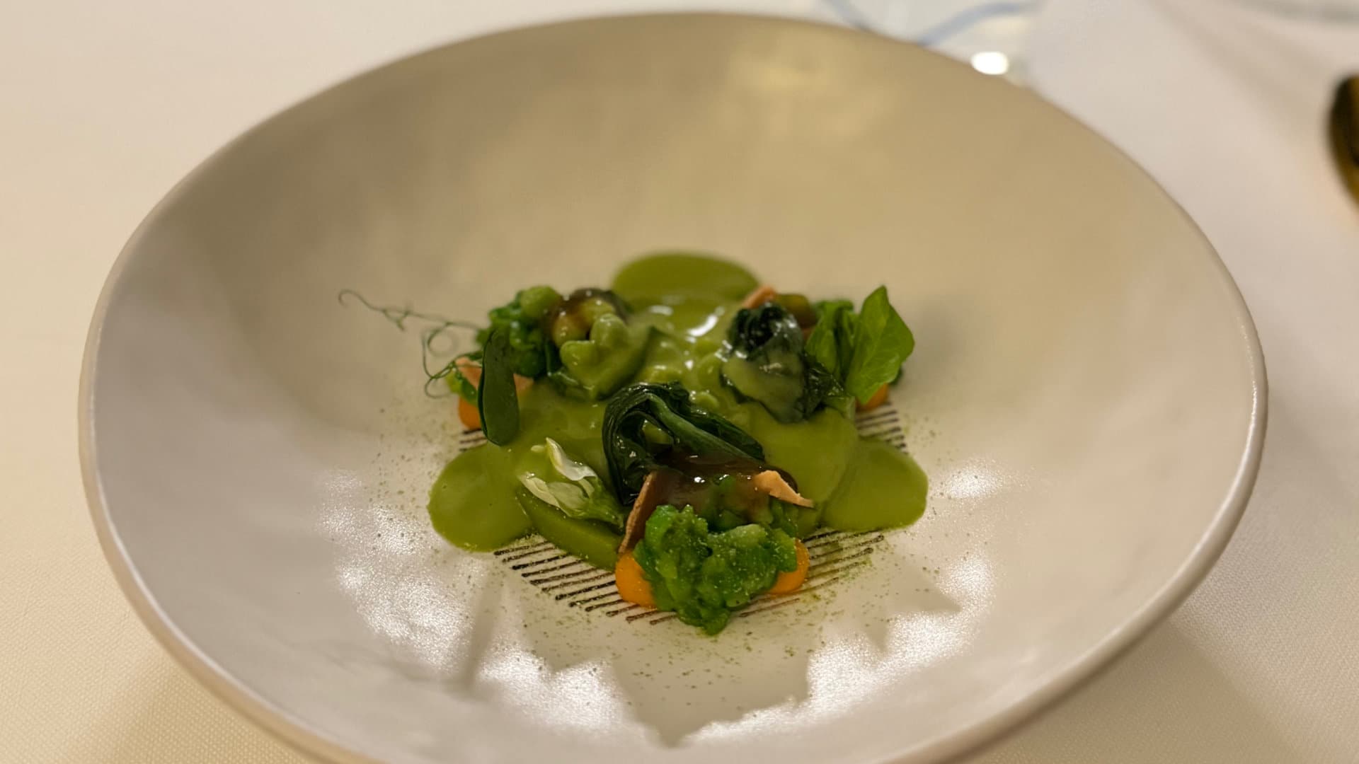 Vibrant green pea purée and herb emulsion styled inside a modern white bowl.
