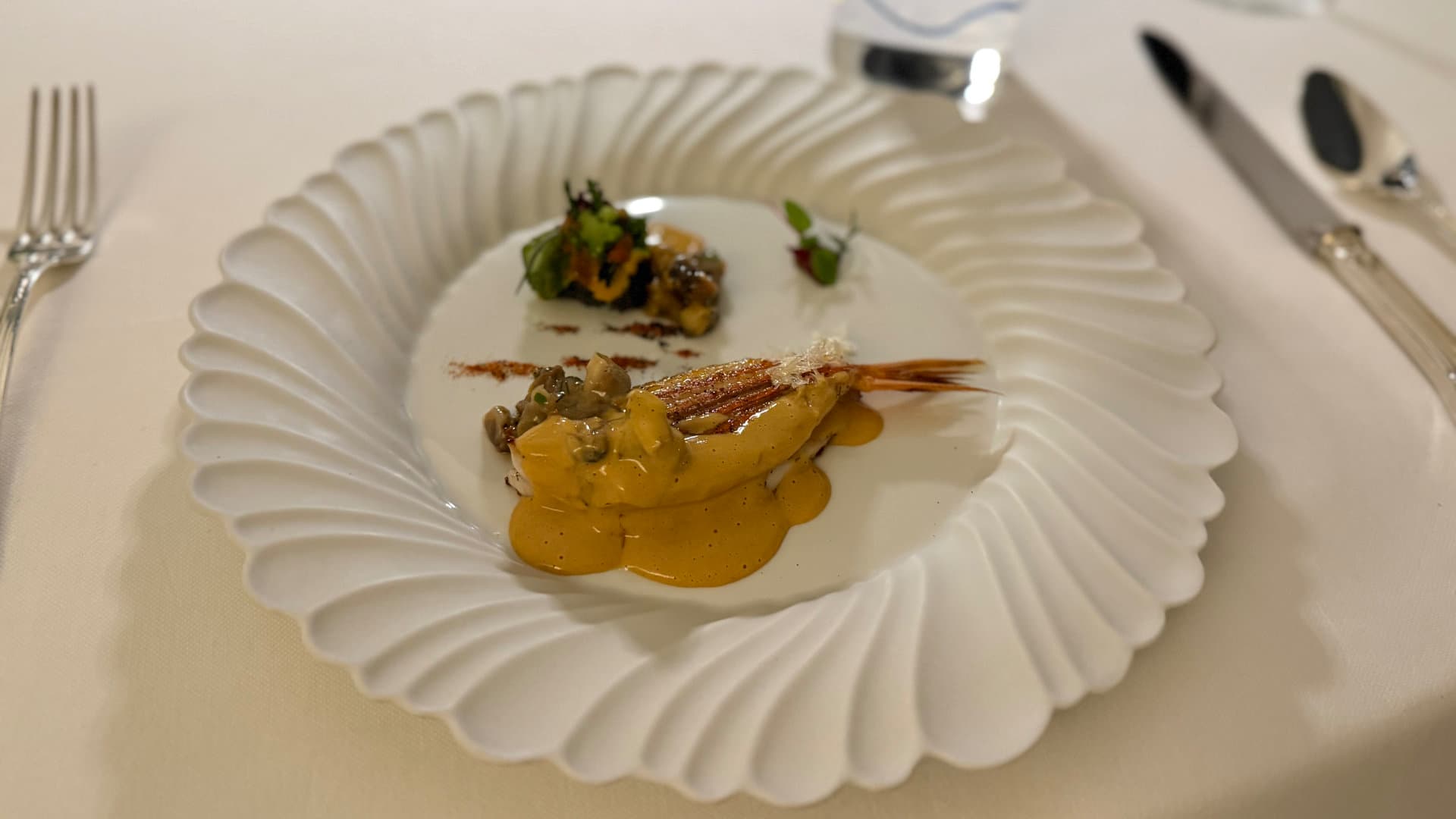 Red mullet fish dish with savory sauce and seaweed garnish on a pleated plate.