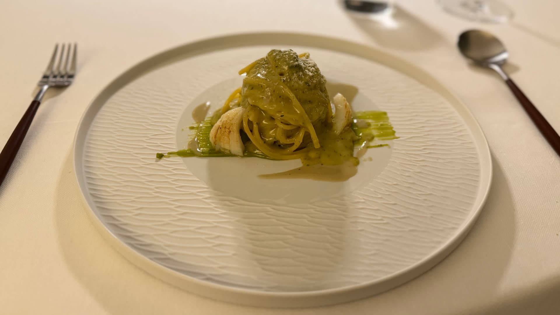 Green pasta twirl garnished with white squid pieces and herb sauce on a white plate.