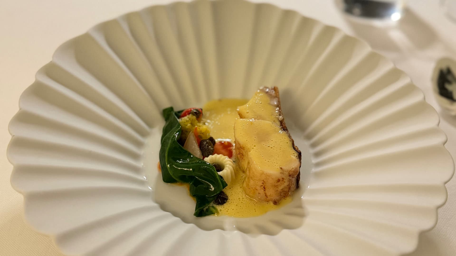 Seared fish fillet with vibrant vegetables and yellow sauce in a shell-shaped bowl.