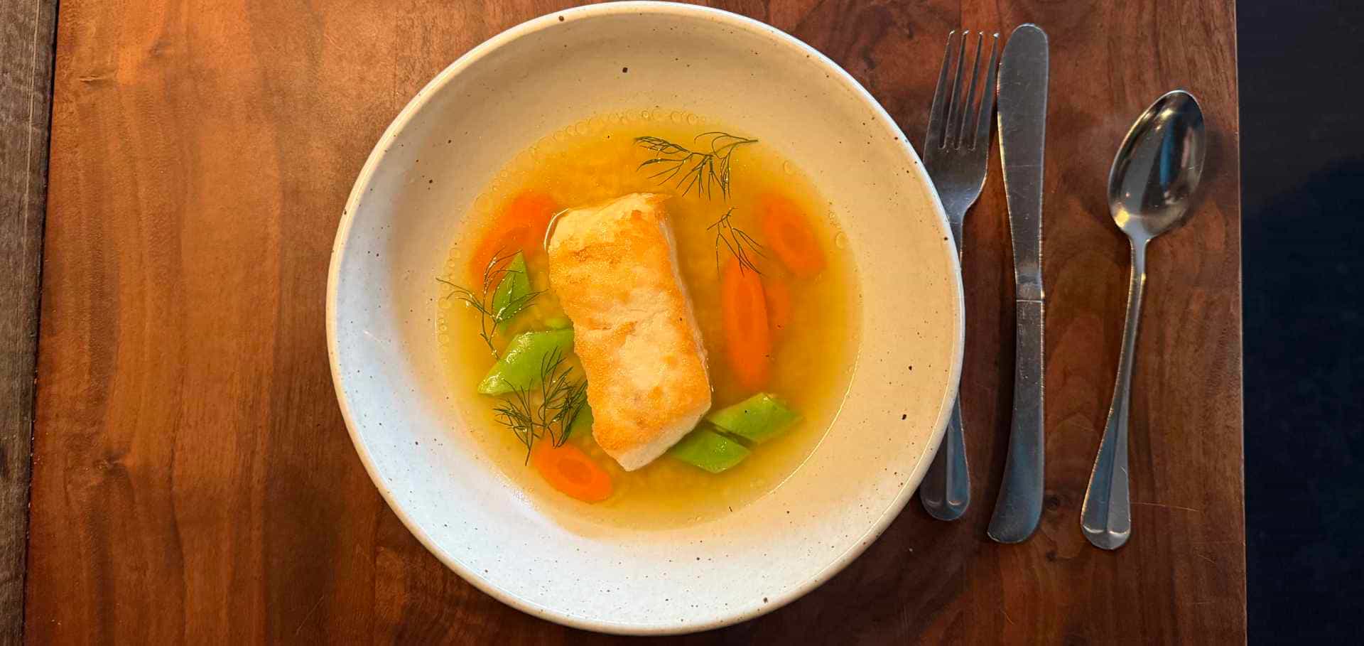 Seared fish fillet served in a clear savory broth with carrots and herbs.
