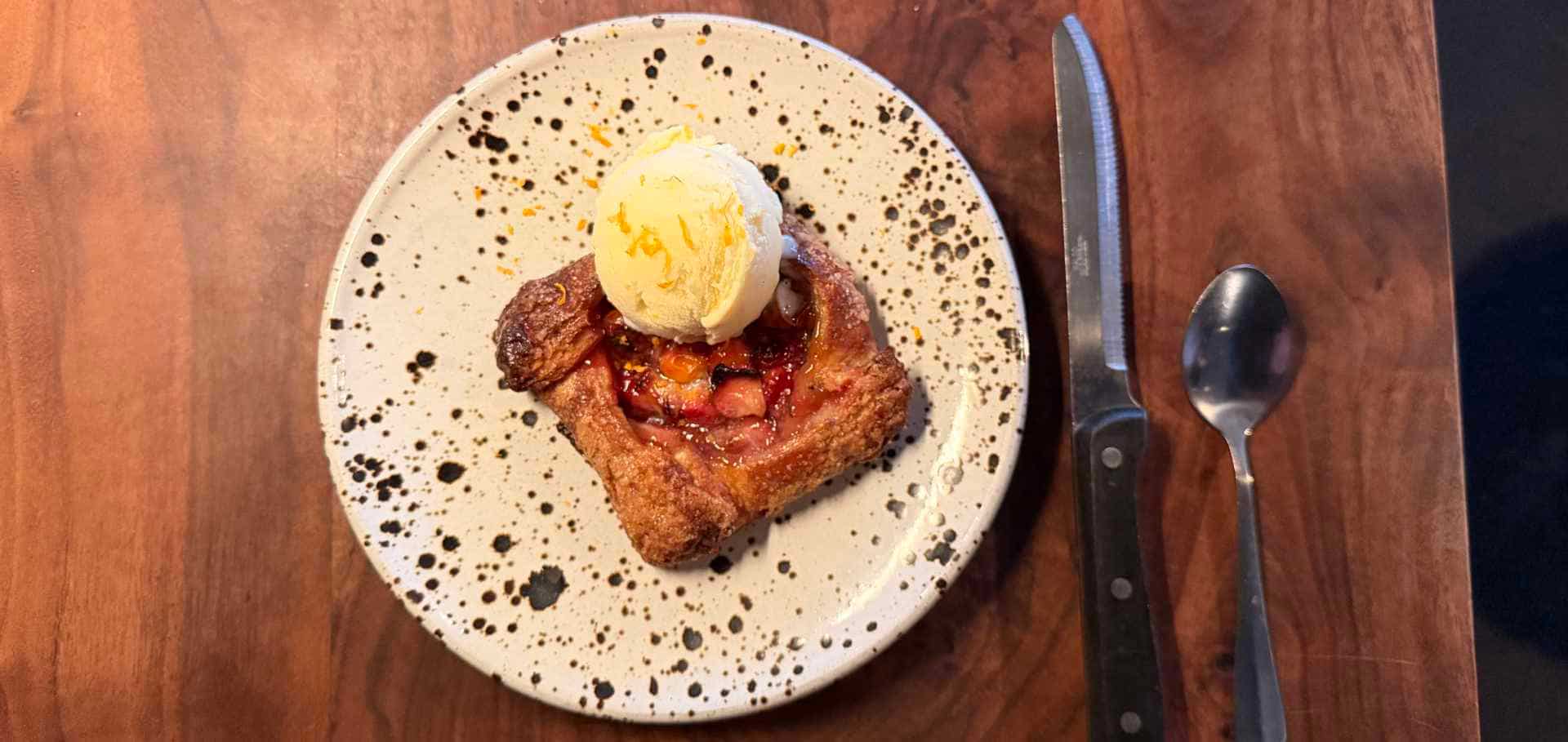 Flaky fruit pastry topped with a scoop of vanilla ice cream and orange zest.
