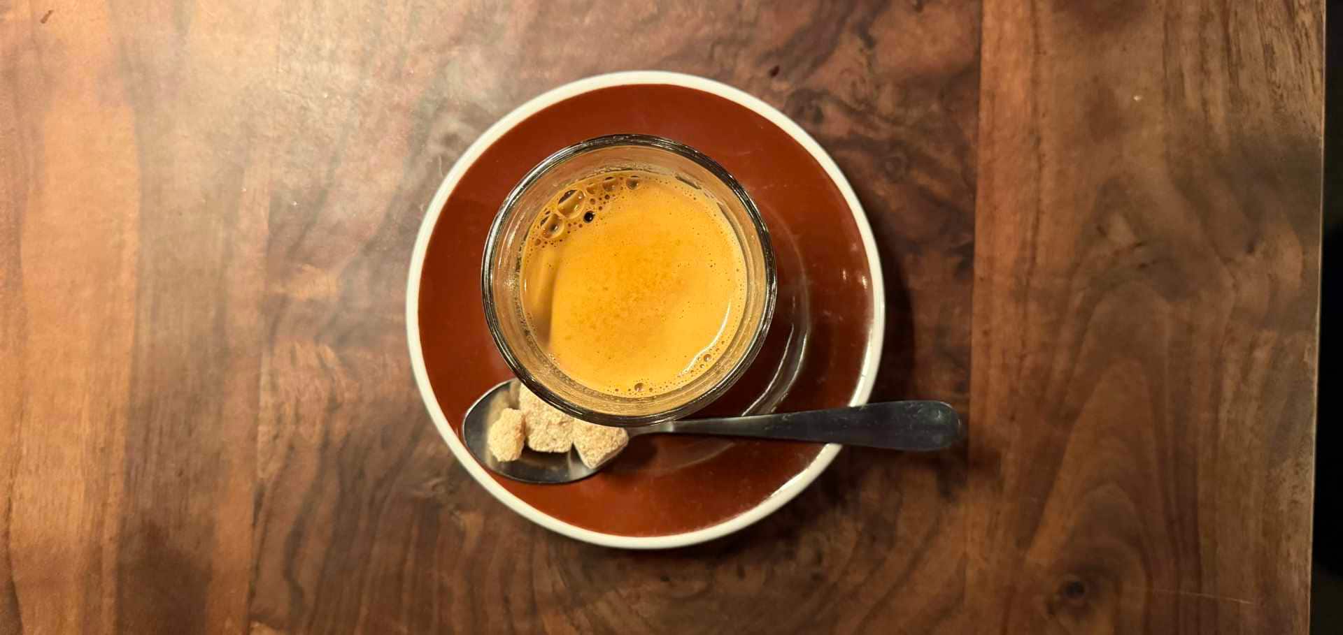 Freshly brewed espresso served in a small glass with brown sugar cubes.