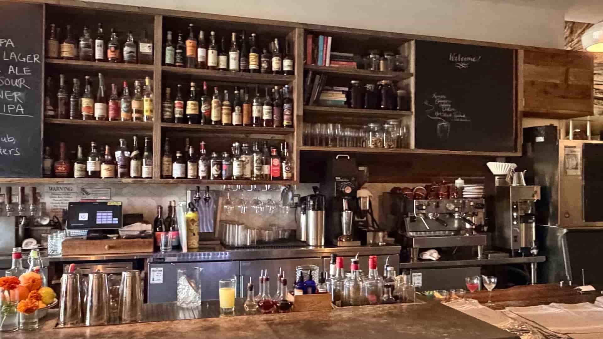 Ambient bar interior featuring wooden walls, chalkboard menus, and modern pendant lights.