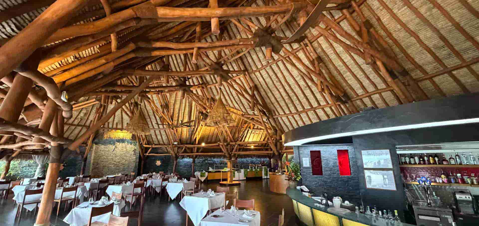 Vaulted timber dining pavilion with white-clothed tables and bar counter.