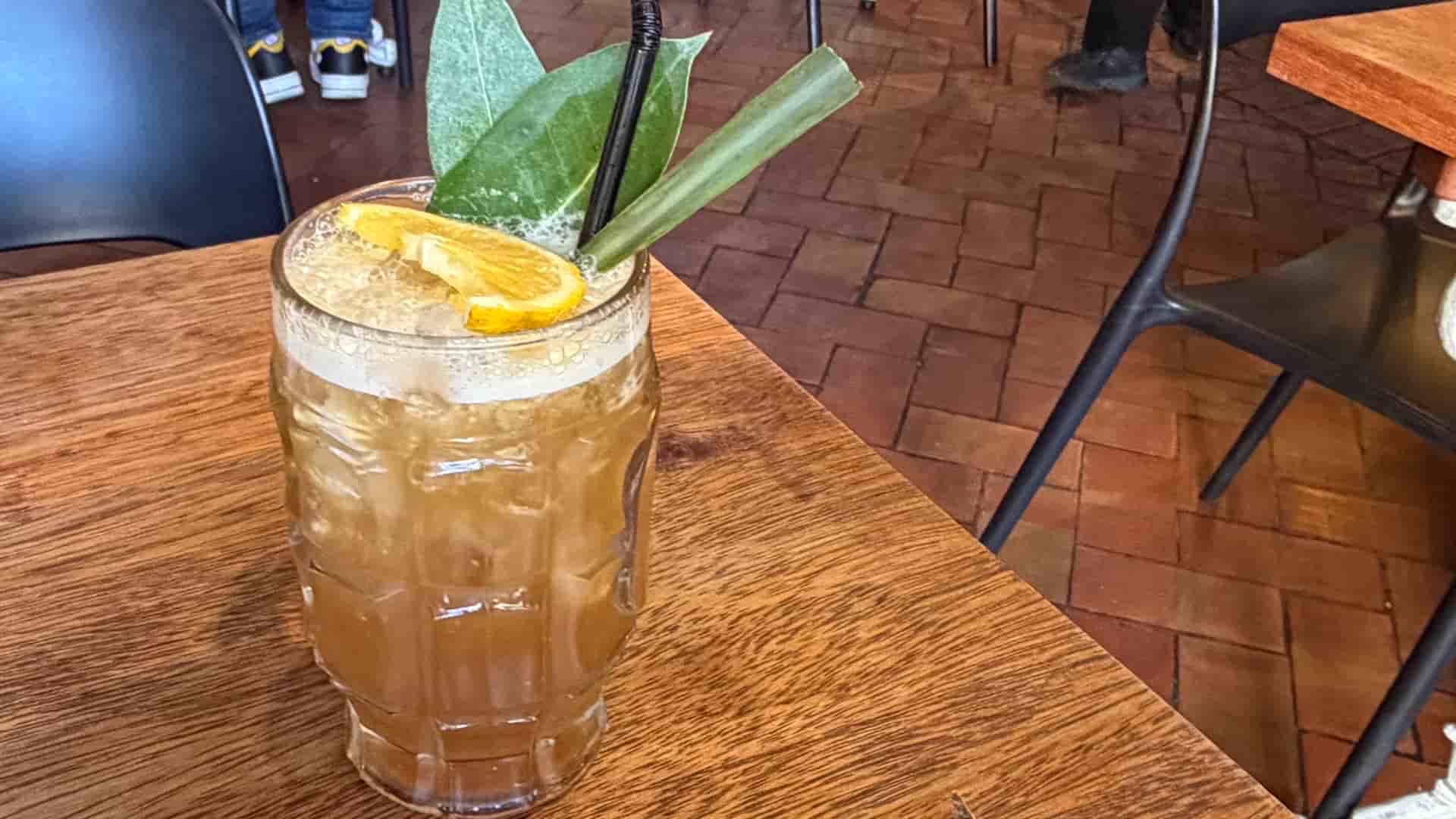 Refreshing local cocktail garnished with citrus and fresh green herbs on a wooden table.
