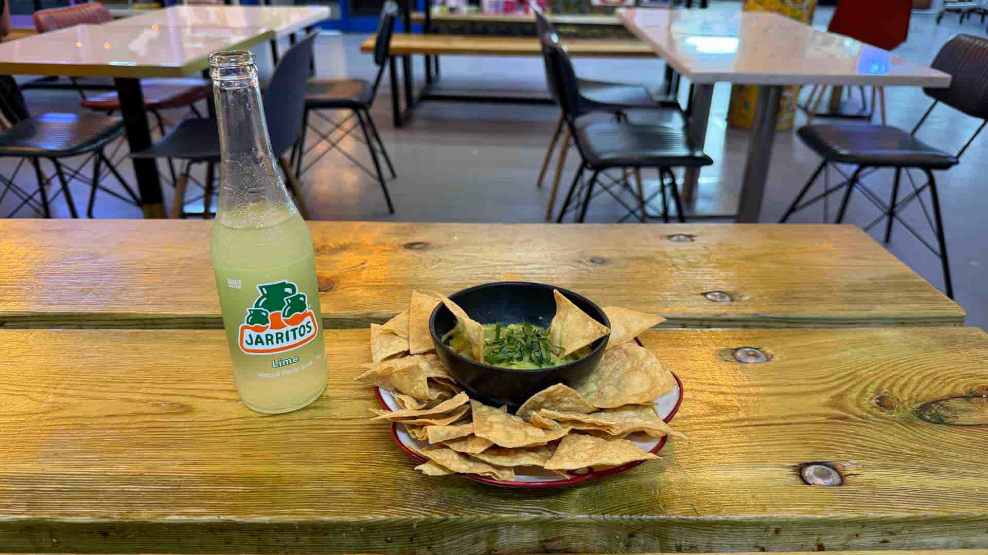 Refreshing glass bottle of Jarritos lime soda beside a bowl of fresh tortilla chips.