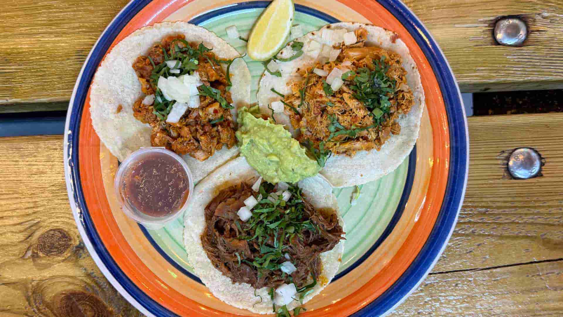 Assorted street tacos served with fresh lime wedges, cilantro, and chunky guacamole.