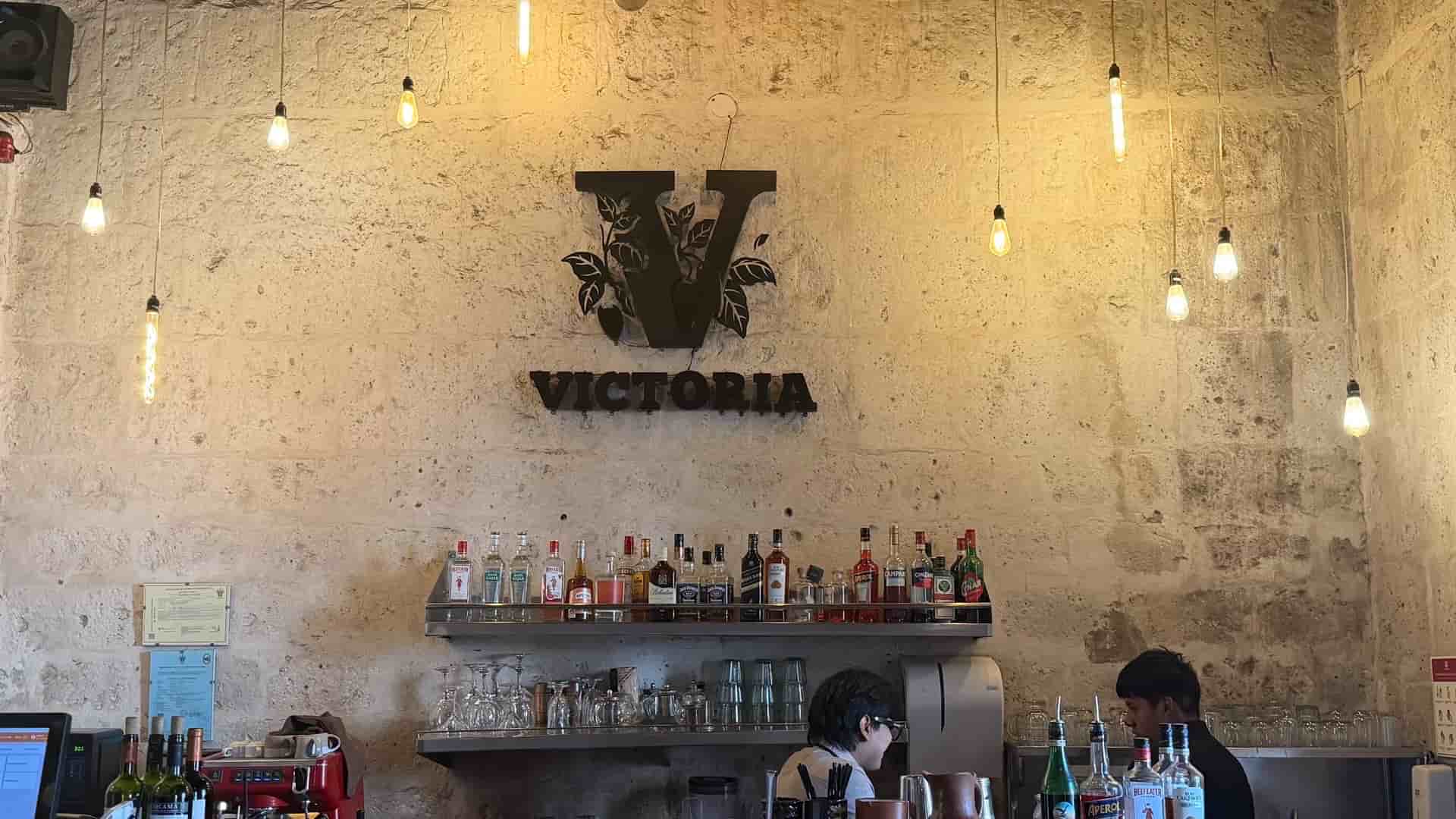 Warm interior bar counter featuring hanging pendant lights and a distinctive V logo wall sign.