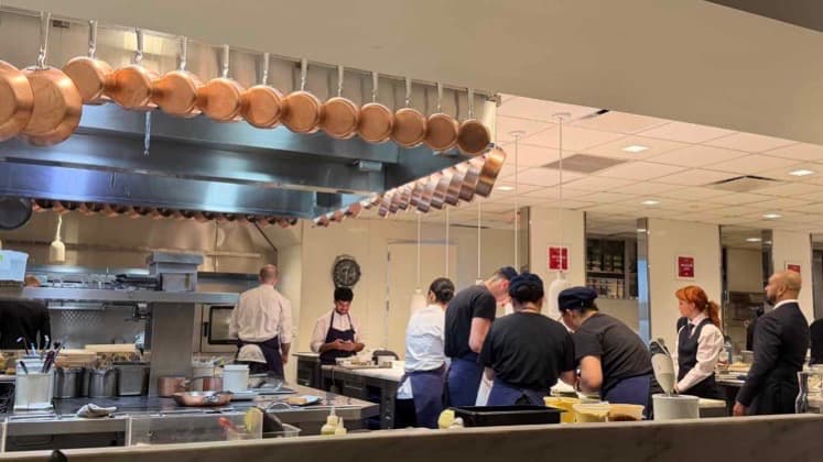 Professional kitchen brigade and service staff working in a sleek stainless steel kitchen.